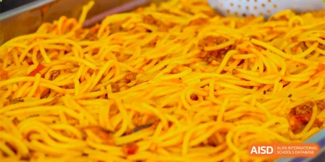 A close-up of a tray filled with spaghetti or long yellow noodles with sauce served at Oriental Cambridge International School's cafeteria.