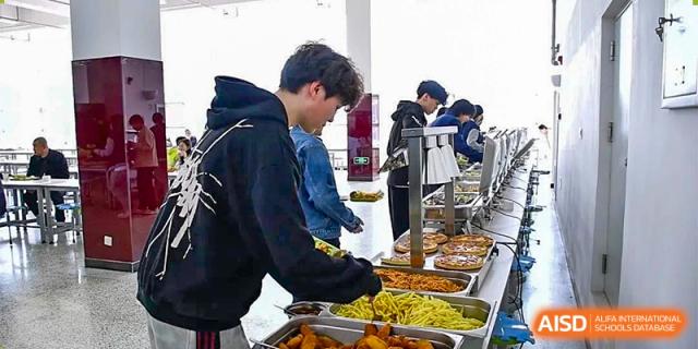 Older students at Oriental Cambridge International School serving themselves from a buffet line filled with various hot food items.