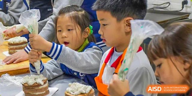 Two young students at Oriental Cambridge International School looking at food, with the boy holding a piece of bread or a pastry with topping.