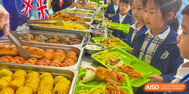 A variety of hot food items, including pastries, corn on the cob, and sausages, displayed on a bright green serving tray at Oriental Cambridge International School.