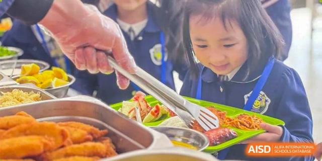A close-up of a student or server at Oriental Cambridge International School using tongs to pick up food from the serving line in the cafeteria.