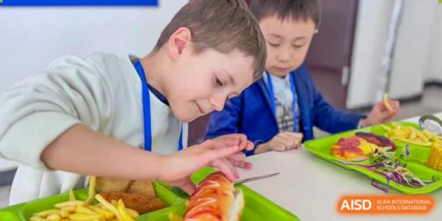 A young, light-haired student at Oriental Cambridge International School smiling and looking at a pastry or food on their plate during a meal.