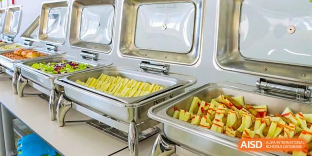 A stainless steel chafing dish at Oriental Cambridge International School containing French fries or potato sticks and other mixed foods.