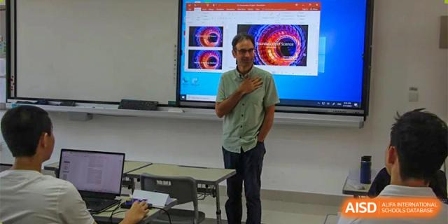 A teacher from RCF Experimental School giving a presentation in a classroom with a large screen.