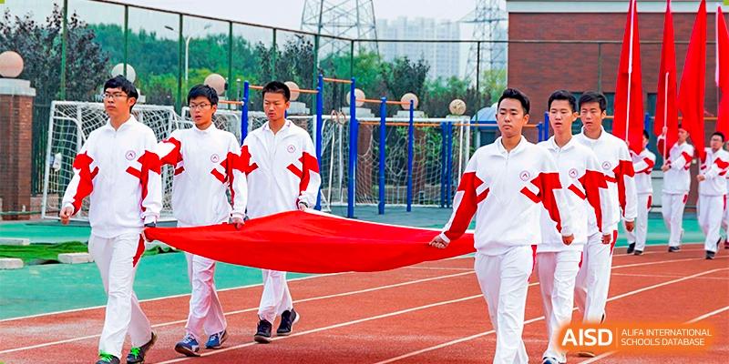 A group of students from RCF Experimental School in white and red uniforms holding a large red banner outdoors.