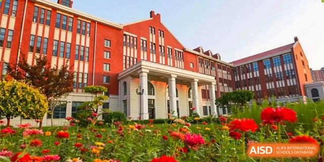The beautiful red-brick campus building of RCF Experimental School surrounded by lush greenery and flowers.