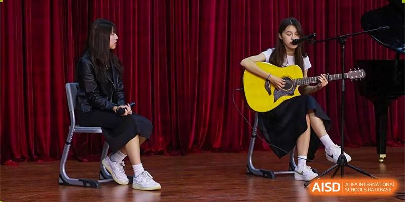 A student from RCF Experimental School playing a guitar on a stage with red curtains.