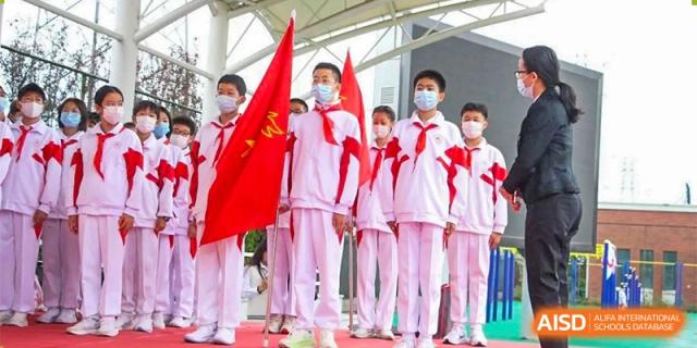 Students from RCF Experimental School in uniform holding red flags during a ceremony.