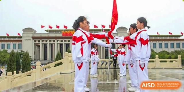 Students from RCF Experimental School standing in uniform and holding red flags outdoors.