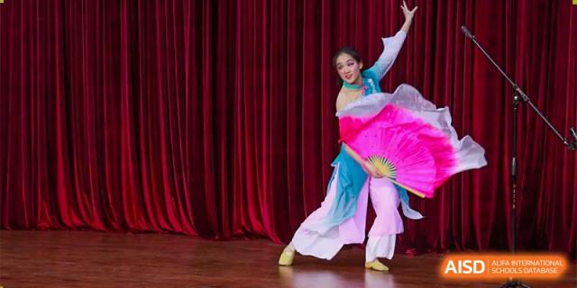 A student from RCF Experimental School performing a traditional dance on a stage with red curtains.