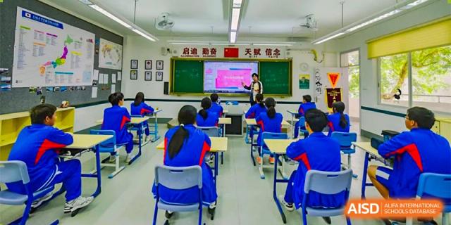 Students sit at individual desks in a bright classroom, watching a digital presentation during a lesson at Guangzhou Yinghao School.