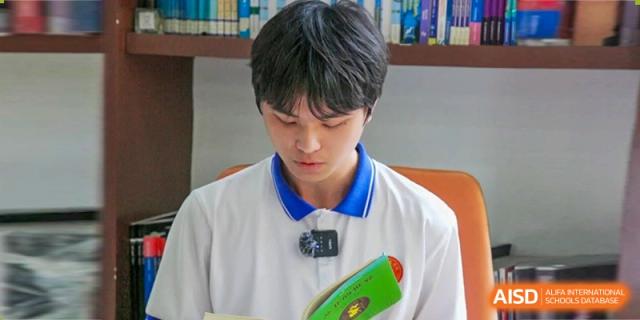 A focused male student in a white polo shirt with blue trim looks down while reading a book during a quiet study period at Guangzhou Yinghao School.
