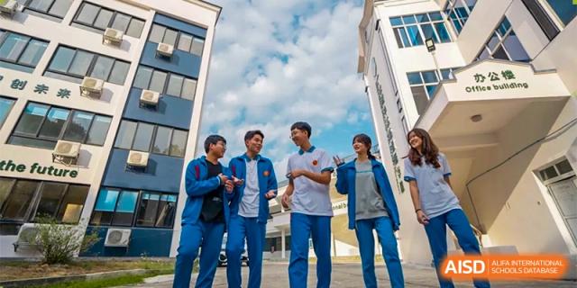 A group of five students in blue and white uniforms walk together and chat outside between modern school buildings at Guangzhou Yinghao School.