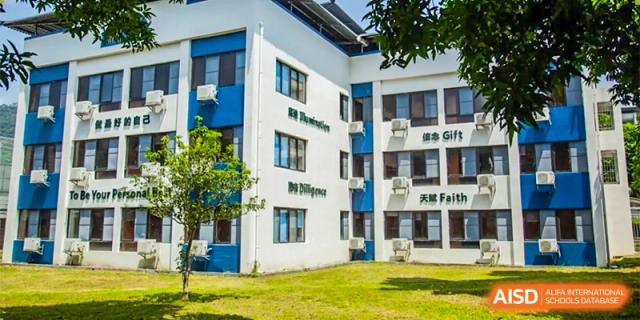 A white academic building features large windows and blue accents, surrounded by green grass and young trees at Guangzhou Yinghao School.