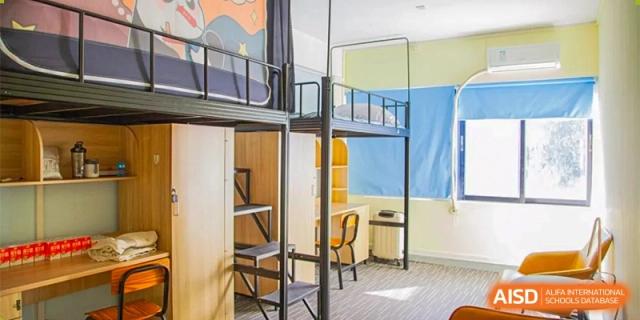 A clean and modern student dormitory room featuring black metal bunk beds with integrated wooden desks and storage shelving at Guangzhou Yinghao School.