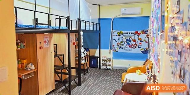 A modern dormitory room featuring black metal loft beds with integrated desks and a cozy seating area at Guangzhou Yinghao School.
