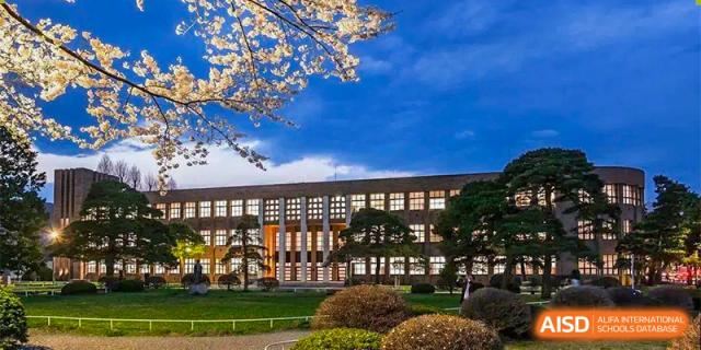 The school’s main academic building is illuminated at dusk, framed by blossoming cherry trees and manicured lawns at Guangzhou Yinghao School.