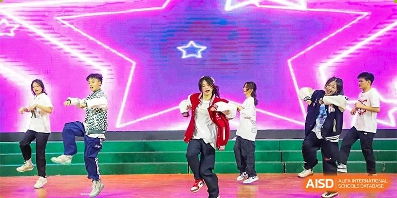 Students perform a modern hip-hop dance routine on a stage with a large glowing pink star backdrop at Guangzhou Yinghao School.