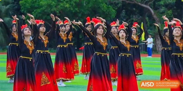 A group of female students in traditional black and red dresses perform a synchronized dance on a green field at Guangzhou Yinghao School.