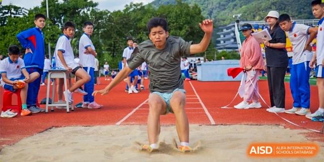 A male student performs a long jump, landing in a sand pit during an outdoor sports competition at Guangzhou Yinghao School.