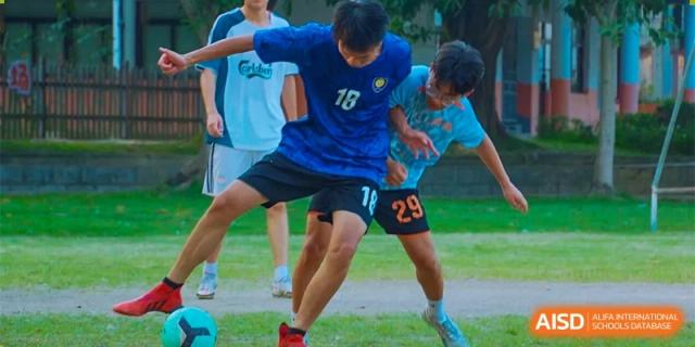 Two students in blue jerseys compete for the ball during an intense soccer match on a grassy field at Guangzhou Yinghao School.