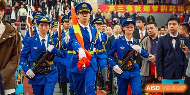 Students in formal blue marching band uniforms carry flags and instruments during a ceremonial school parade at Guangzhou Yinghao School.
