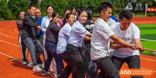 A group of teachers and staff participate in a competitive tug-of-war match on a red athletic track at Guangzhou Yinghao School.