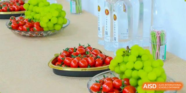 Trays of fresh red cherry tomatoes and green grapes are arranged on a table for a school event or snack time at Guangzhou Yinghao School.