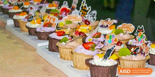 A row of decorative cupcakes topped with purple frosting, fresh strawberries, and Halloween-themed paper toppers at Guangzhou Yinghao School.
