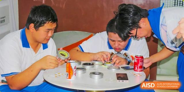 Two students sit at a table and work meticulously on a small-scale craft or assembly project during a hands-on activity at Guangzhou Yinghao School.