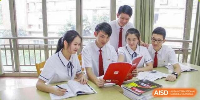 A group of students in school uniform collaboratively studying a red book at a desk at Guangdong Experimental High School IFPAD & A-Level.