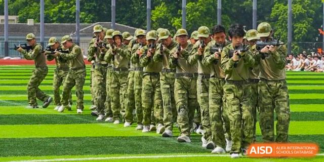 A line of students in camouflage uniforms marching or standing in formation during military training at Guangdong Experimental High School IFPAD & A-Level.
