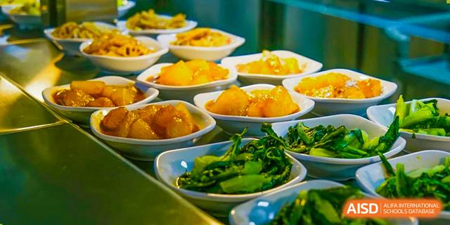 A selection of small bowls containing side dishes, including cooked green vegetables and what appears to be stewed fruit, served at Guangdong Experimental High School IFPAD & A-Level.