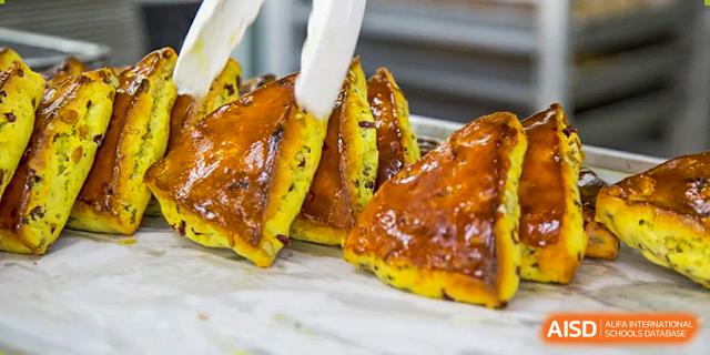 Tongs holding a slice of golden-brown, glazed pastry or bread product, part of the meal offerings at Guangdong Experimental High School IFPAD & A-Level.