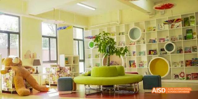 A bright and modern reading area with a unique green circular sofa and large potted plant next to shelves of books, at Beanstalk International Bilingual School.