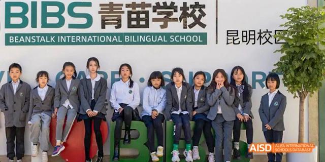 A group of six young female students sitting outdoors on a ledge in front of a banner that reads "ONAL BILINGUAL SCHOOL," at Beanstalk International Bilingual School.