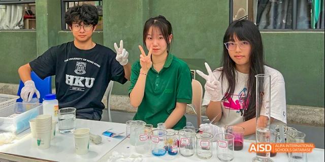 A female student in a green polo shirt giving a peace sign while participating in a hands-on science experiment with beakers and liquids, at Beanstalk International Bilingual School.