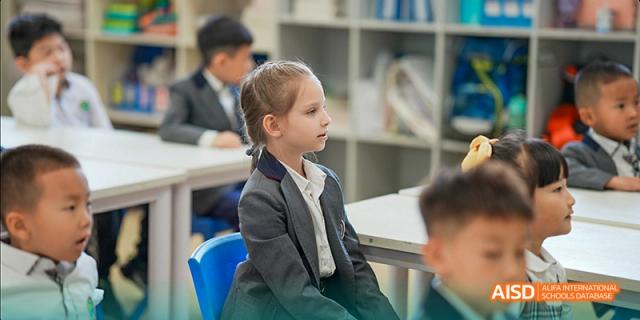 A young female student in a grey suit and tie uniform sitting attentively in a classroom, looking forward during a lesson, at Beanstalk International Bilingual School.