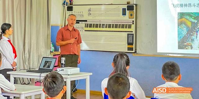 A teacher in an orange shirt instructing a small group of students in a classroom with a large keyboard chart on the wall, at Beanstalk International Bilingual School.