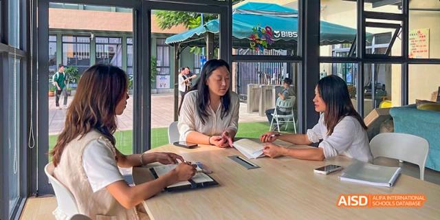 An outdoor shot of a female student in a white shirt studying or having a discussion at a table with other students, at Beanstalk International Bilingual School.