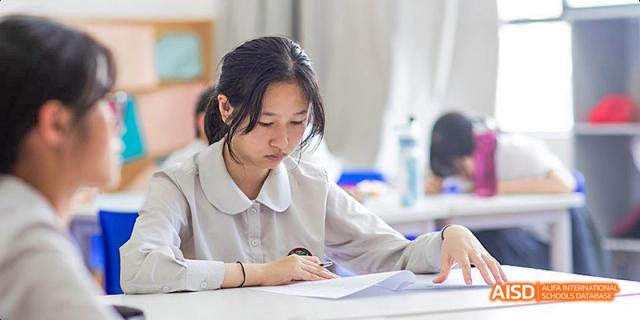 A female student in a white uniform shirt intently writing or studying with papers spread out on a desk, at Beanstalk International Bilingual School.