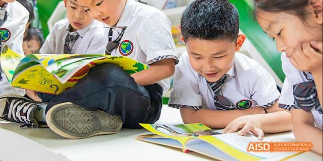 Two young male students sitting on the floor together, closely reading and collaborating on a bright yellow open textbook, at Beanstalk International Bilingual School.