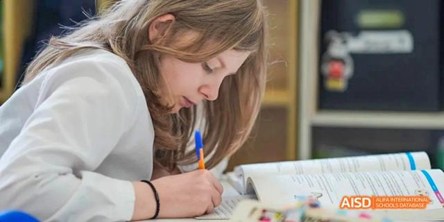 A female student with blonde hair intently writing in a notebook or textbook during a focused study session, at Beanstalk International Bilingual School.