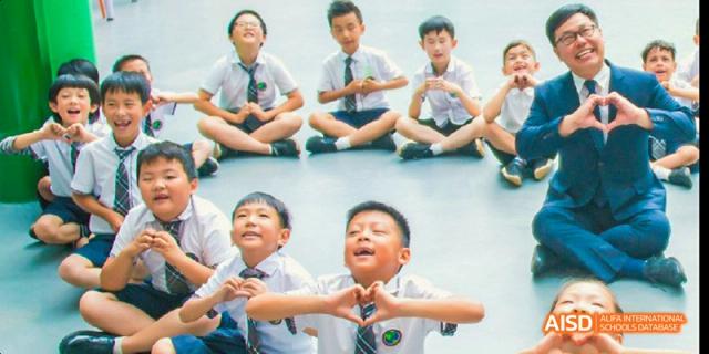 A group of young male students in school uniform sitting down, with one student in the foreground forming a heart shape with his hands, at Beanstalk International Bilingual School.