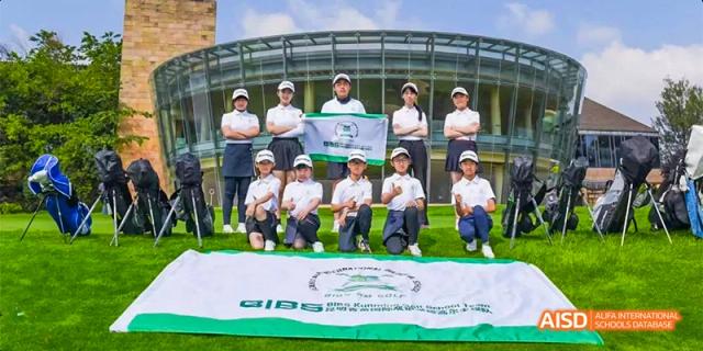 A group of students and teachers in white shirts posing with a large green and white banner on a sports field, at Beanstalk International Bilingual School.