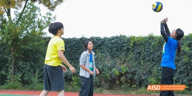 Two students, one in a yellow shirt and one in a light gray jacket, walking on a track next to a hedge, at Beanstalk International Bilingual School.