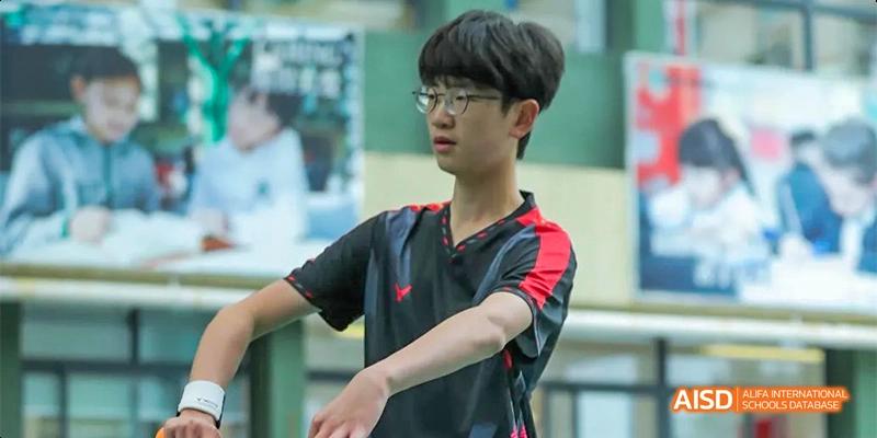 A male student wearing glasses and a red and black shirt is focused on a sports activity, with his arms extended, at Beanstalk International Bilingual School.
