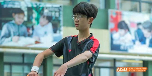 A male student wearing glasses and a red and black shirt is focused on a sports activity, with his arms extended, at Beanstalk International Bilingual School.