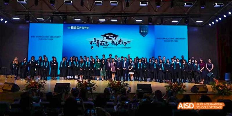 A group of students and teachers on a stage, standing in front of a blue backdrop with school logos and graduation text, at Beanstalk International Bilingual School.