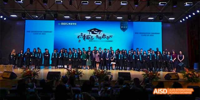 A group of students and teachers on a stage, standing in front of a blue backdrop with school logos and graduation text, at Beanstalk International Bilingual School.